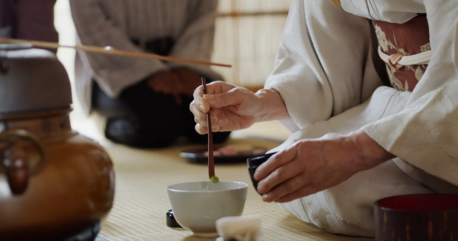 A kimono-clad host scooping matcha in a tatami tea room